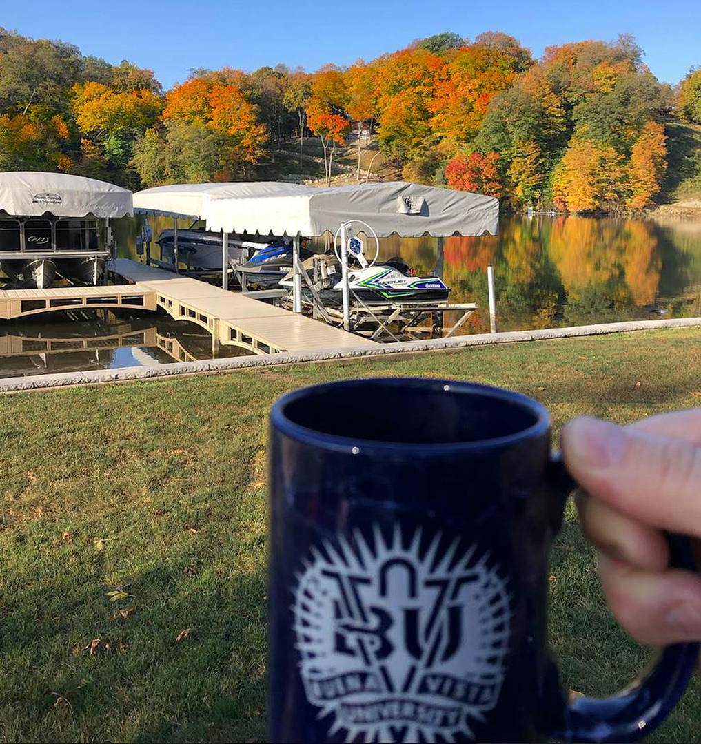 Hand holding a coffee mug looking out to a lake with fall foliage