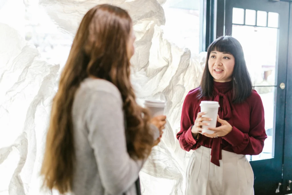 business professional women stand in a cafe with coffee, speaking to one another