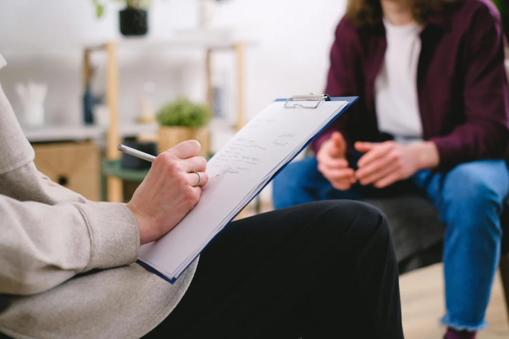 two women sit across from one another, one writes on clipboard